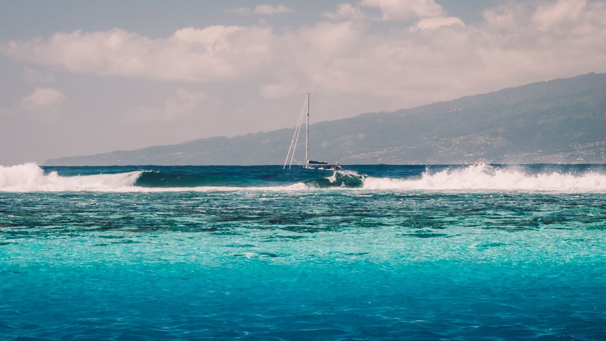 sailboat crashing through the waves outside of the barrier reef in moorea french polynesia